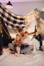Father and his kids reading book together while sitting in handmade tent in children's room
