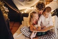 Father and his kids reading book together while sitting in handmade tent in children's room