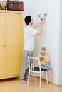 Father with a small toddler son are attaching framed drawing to the wall