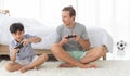 Father and his mixed-race son holding controller joystick to play a game together with fun and happy in bedroom Royalty Free Stock Photo