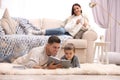 Father and his son reading books while mother resting on sofa at home