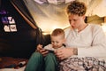 Father and his son watching cartoons on tablet while sitting in handmade tent in children's room