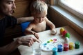 Father and his toddler blond son dyeing Easter eggs together at home