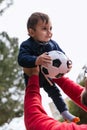 Father holding his little son up in the air with a soccer ball while playing together outdoors in the park. Royalty Free Stock Photo
