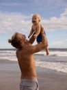 Father holding and lifting his infant baby boy high in the air on beach. Positive emotions. Dad and son laughing and smiling. Blue Royalty Free Stock Photo