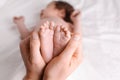 Father holding newborn baby boy feet in bedroom, closeup of barefoot in a selective focus Royalty Free Stock Photo