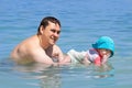 Father holds smiled child in the water and teaches to swim. Summer vacation on tropical beach. Infant baby girl 9 month first time Royalty Free Stock Photo