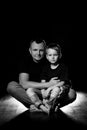 Father holds son in his arms and hugs him. Man and boy are sitting together against a black background. Happy fatherhood and Royalty Free Stock Photo