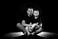 Father holds son in his arms and hugs him. Man and boy are sitting together against a black background. Happy fatherhood and Royalty Free Stock Photo