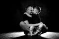 Father holds son in his arms and hugs him. Man and boy are sitting together against a black background. Happy fatherhood and Royalty Free Stock Photo