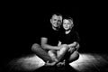 Father holds son in his arms and hugs him. Man and boy are sitting together against a black background. Happy fatherhood and Royalty Free Stock Photo