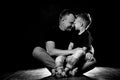 Father holds son in his arms and hugs him. Man and boy are sitting together against a black background. Happy fatherhood and Royalty Free Stock Photo