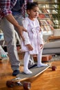 A father at home teaches his little daughter how to ride a skateboard. Family, home, playtime