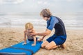 Father or instructor teaching his 4 year old son how to surf in the sea on vacation or holiday. Travel and sports with