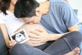 Father is kissing his mother`s stomach. Young husband kissing his pregnant wife`s tummy in living room with the baby ultrasound