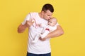 Father kissing newborn daughter or son while holding feeding bottle and soother in hands, guy wearing casual attire, standing Royalty Free Stock Photo
