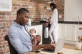 Father On Laptop Holds Newborn Son As Mother Makes Meal Royalty Free Stock Photo