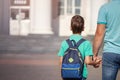 Father leads a little child school boy go hand in hand. Parent and son with backpack behind the back