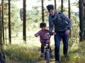 Father learning his son to ride on bicycle outside, real happy family in summer forest enjoing nature