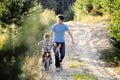 Father learning his son to ride on bicycle outside, real happy family in summer forest enjoing nature