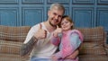 Father and little child daughter kid in pajamas sit on couch in room smiling, showing thumbs up Royalty Free Stock Photo