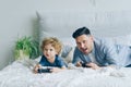 Father and child playing video game on bed at home pressing buttons on joystick