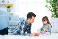 Father and little daughter having quality family time together at home. dad with girl lying on warm floor drawing with colorful Royalty Free Stock Photo