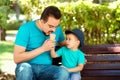 Father and little son eating ice-cream together in park in sunny summer or autumn day. Boy offers ice-cream to daddy. Happy family