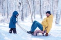 Father and toddler son having good time together in winter park: dad is sitting in sledge and child is trying to pull him Royalty Free Stock Photo