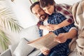 Father and little son at home boy hugging dad sitting on sofa reading newspaper together relaxed Royalty Free Stock Photo