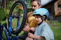 Father with little son together preparing bicycle for a ride, pumping up tyres in garden in front of house.