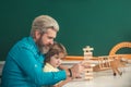 Father looking at son playing jenga game. Cute pupil and his father in classroom. Supporting pupils at school Royalty Free Stock Photo