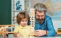 Father looking at son playing jenga game. Little boy pupil with happy face expression near desk with school supplies Royalty Free Stock Photo