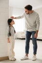 Father measuring daughter`s height near white brick pillar at home