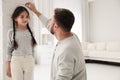 Father measuring daughter`s height near white brick pillar at home