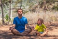 Father meditates yoga pose close eyes in forest park fresh air, son repeats but tired waiting look in parent face angry