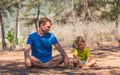 Father meditates yoga pose in forest park on fresh air, son repeats but tired waiting look down. Daddy influence on boy Royalty Free Stock Photo