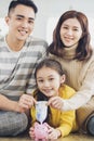 Father, mother and daughter holding piggy bank and money at home. Family and saving for future concept Royalty Free Stock Photo