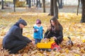 Father, mother and his little son rest in autumn garden. Cute boy playing with the toy car in the autumn park. Royalty Free Stock Photo