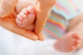 Father or mother holding foot of newborn baby. Adult hand and baby tiny baby feet. Happy parenthood, carefree childhood