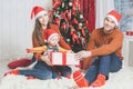 Father, mother and infant holding Cristmas gift near Christmas tree