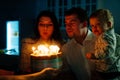 a father and mother with a kid son make a wish and blow out candles on the cake. Royalty Free Stock Photo