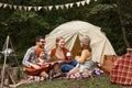 Father, mother and little son sitting near tourist tent and playing guitar during camping Royalty Free Stock Photo