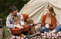 Father, mother and little son sitting near tourist tent and playing guitar during camping Royalty Free Stock Photo