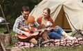 Father, mother and little son sitting near tourist tent and playing guitar during camping Royalty Free Stock Photo