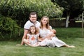 Father, mother and two children, baby girl and little daughter on the grass on summer day. Happy family sitting together outdoors Royalty Free Stock Photo