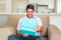Middle-aged man wearing light blue shirt opening turquoise gift box in open-plan kitchen with smile Royalty Free Stock Photo
