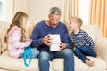Father opening gift given by children on sofa Royalty Free Stock Photo