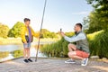 father photographing son with fishing rod on river