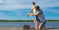 Father on the pier helps his son to keep a fishing rod for fishing, against the blue lake and sky Royalty Free Stock Photo
